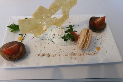 Assiette gastronomique avec macaron salé, légumes garnis, mousse blanche, tuile croustillante et décorations herbacées.