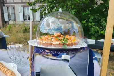 Plateau de bouchées apéritives sous une cloche en verre, présenté sur une table en extérieur près d'un bâtiment ancien.