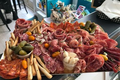Plateau de charcuterie variée avec cornichons, gressins, tomates cerises et ail mariné, présenté sur un comptoir.