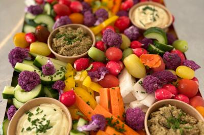 Plateau de crudités colorées avec carottes, concombres, tomates, chou-fleur violet et sauces variées en petits bols.