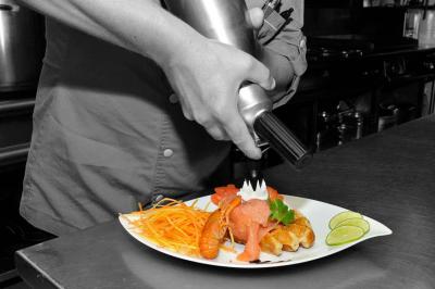 Un chef décore un plat de saumon, crevettes et légumes avec une mousse à l'aide d'un siphon en cuisine professionnelle.