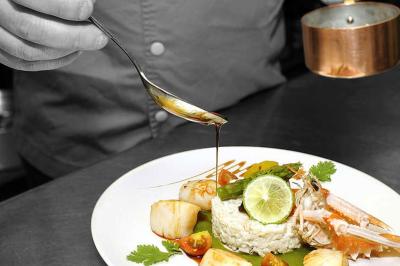 Un chef verse une sauce sur un plat raffiné composé de riz, fruits de mer, légumes et citron vert.