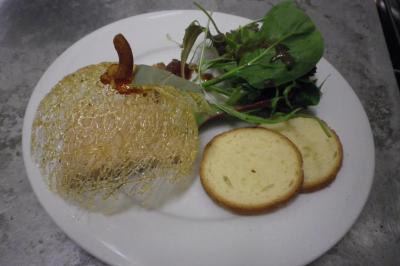 Assiette contenant un foie gras décoré de caramel filé, accompagné de toasts et d'une salade verte.