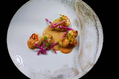 Assiette gastronomique avec crevettes, sauce crémeuse et garniture de légumes colorés sur une présentation soignée.