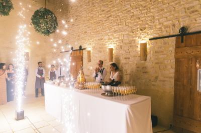 Table de réception avec champagne, pièce montée et invités dans une salle en pierre éclairée par des lumières festives.