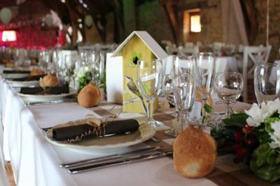 Table dressée pour un repas festif dans une salle rustique, avec décorations florales et pain individuel.