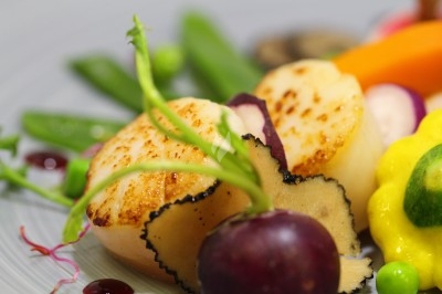 Noix de Saint-Jacques poêlées accompagnées de légumes colorés, truffes et touches de sauce sur une assiette.
