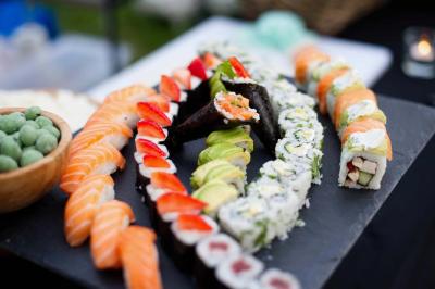 Assortiment de sushis variés disposés sur une ardoise, avec des garnitures colorées et une coupe de wasabi à côté.