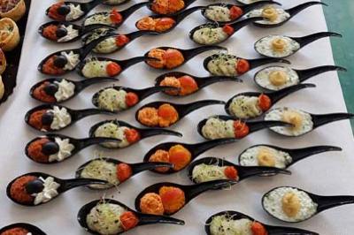 Présentation de cuillères apéritives variées disposées en rangées sur une nappe blanche, accompagnées de bouchées sucrées.