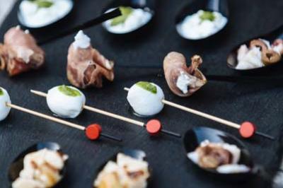 Assortiment de bouchées apéritives sur un plateau noir, comprenant brochettes et cuillères garnies.