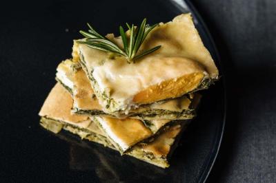 Tranches de quiche aux légumes et fromage empilées sur une assiette noire, garnies d'une branche de romarin.