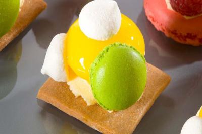 Pâtisserie composée d'un biscuit, d'une crème jaune brillante, de meringues blanches et d'un macaron vert.