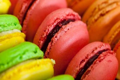 Macarons colorés alignés de près, avec des nuances de rose, jaune et vert, garnis d'une crème au centre.