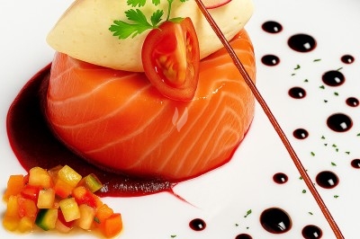 Assiette gastronomique avec saumon fumé, purée, légumes colorés et décorations de sauce artistique.