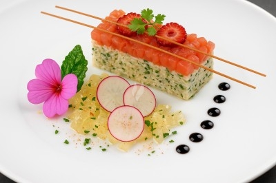 Plat raffiné avec tartare de saumon, radis, gelée, fleur comestible et points de sauce balsamique sur assiette blanche.