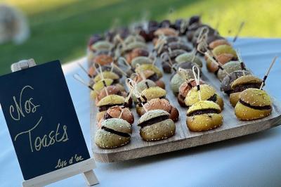 Plateau de mini-burgers colorés alignés sur une table, avec un tableau noir indiquant ’Nos toasts’.
