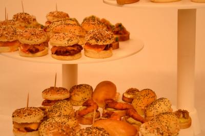Plateaux de mini-burgers et amuse-bouches variés disposés sur des présentoirs blancs.