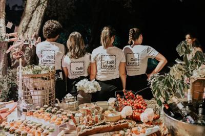 Quatre personnes de dos portant des t-shirts assortis, devant une table garnie de plats et boissons en extérieur.