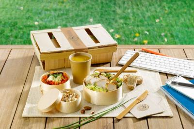 Repas sain présenté dans des contenants en bois sur une table en extérieur, avec clavier et carnet à proximité.