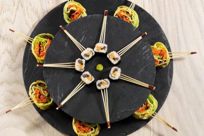 Assortiment de sushis et rouleaux de légumes disposés en cercle sur des plateaux en ardoise avec des baguettes.