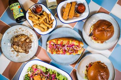 Assortiment de plats comprenant burgers, hot-dog, salade, frites, mozzarella sticks, dessert et boissons sur une table…