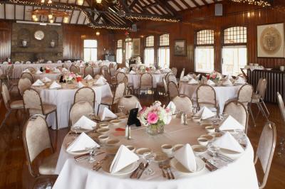 Salle de réception avec tables rondes dressées, nappes blanches, serviettes pliées et centres de table fleuris.