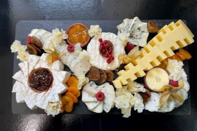 Plateau de fromages variés avec fruits secs, confitures et décorations sur une ardoise noire.