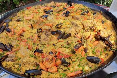 Grande poêle de paella garnie de riz, crevettes, moules, morceaux de viande, légumes et épices.