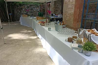 Tables dressées en extérieur avec nappes blanches, contenant verres, paniers de pain et divers éléments pour un buffet.