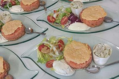 Assiettes avec tartares de saumon, salade verte, tomates cerises, sauce blanche et verrines d'accompagnement.