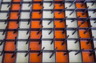 Grille métallique avec des tiges verticales, posée sur des carreaux orange et beige en alternance.