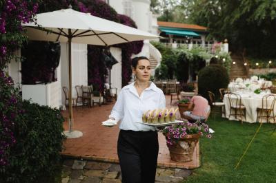 Une serveuse portant des verrines sur un plateau dans un jardin aménagé pour un événement en plein air.