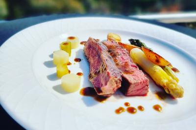 Assiette gastronomique avec viande grillée, asperges, pommes de terre et sauce, présentée sur une table élégante.