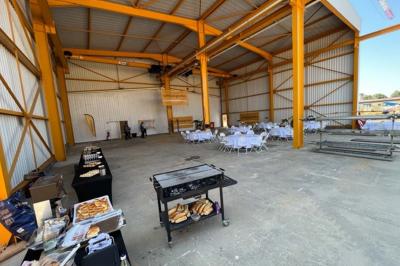 Salle industrielle avec tables rondes dressées pour un événement et buffet installé sur le côté.