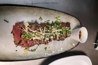 Tranche de viande grillée garnie de ciboulette, cacahuètes et graines, servie avec une sauce à part.