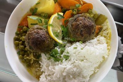 Assiette de riz blanc accompagnée de boulettes de viande, légumes mijotés, pois verts et tranche de citron.
