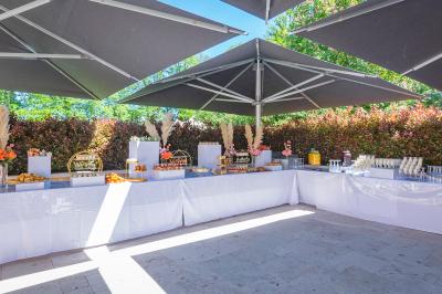 Table de buffet décorée avec des mets variés, installée sous des parasols dans un espace extérieur entouré de verdure.