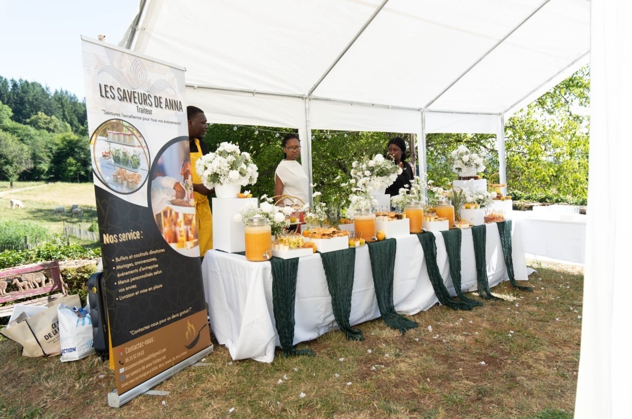 Traiteur Les Saveurs de Anna Traiteur Décines-Charpieu #1 Stand de buffet sous une tente blanche, décoré de fleurs et boissons, avec trois personnes en arrière-plan.