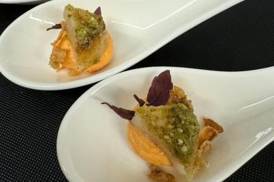 Deux cuillères en porcelaine contenant une bouchée de poisson, crème orange, herbes et éclats croustillants.