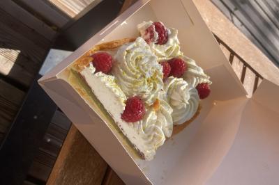 Part de tarte garnie de crème chantilly, framboises fraîches et éclats de pistache, présentée dans une boîte en carton.