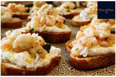 Tranches de pain garnies de fromage frais, crevettes et herbes, disposées sur une surface mouchetée.