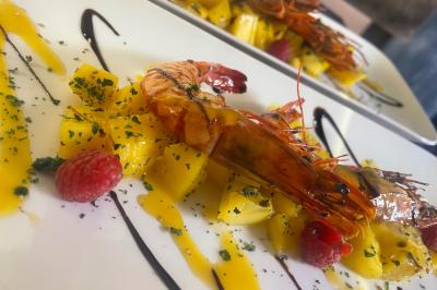 Crevettes grillées servies avec mangue, framboises, herbes fraîches et filet de sauce balsamique sur une assiette blanche.