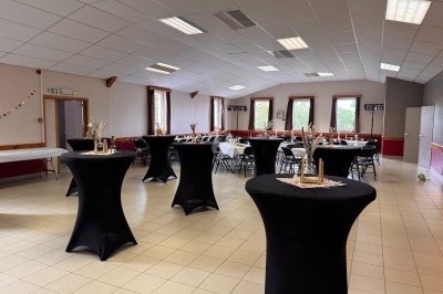 Salle de réception aménagée avec des tables hautes noires et des décorations, éclairée par des fenêtres.