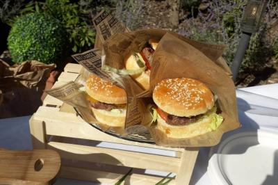 Trois hamburgers servis dans des emballages en papier, présentés sur un plateau en bois dans un cadre extérieur.