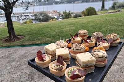 Plateau de canapés variés présenté en extérieur avec vue sur un jardin, un port et une étendue d'eau.