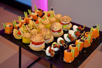 Plateau de bouchées apéritives variées comprenant mini-burgers, roulés de légumes et autres amuse-bouches colorés.