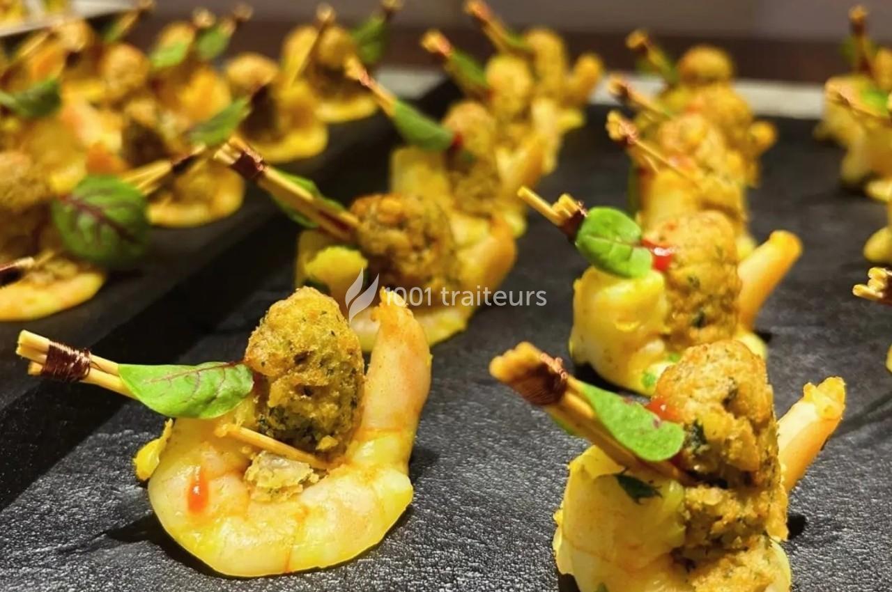 Crevettes garnies de boulettes épicées et décorées de feuilles vertes, présentées sur un plateau noir.