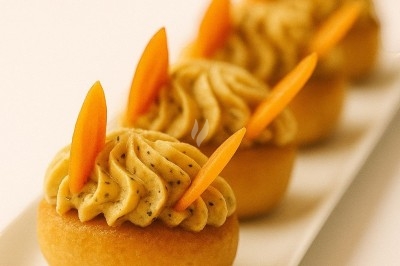 Quatre petits gâteaux décorés de crème et de tranches de fruits orange, présentés sur un plat blanc.