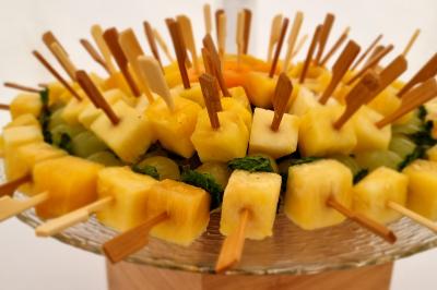 Brochettes de fruits frais avec morceaux d'ananas et de melon, disposées en cercle sur un plat en verre.