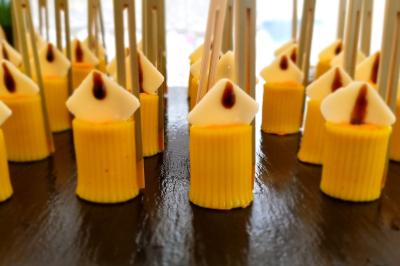 Petits desserts jaunes en forme de bougies avec des bâtonnets, disposés sur une surface sombre.